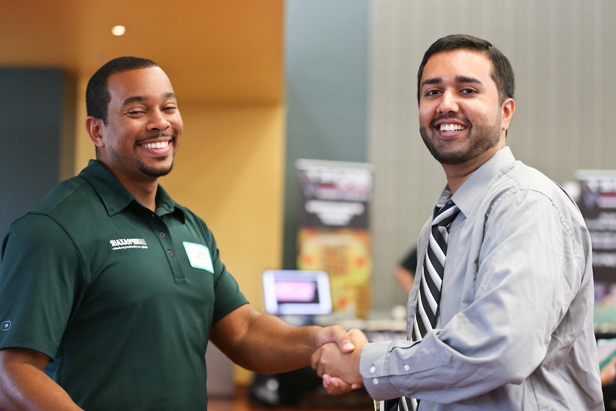 two males shaking hands and looking at the camera and smiling